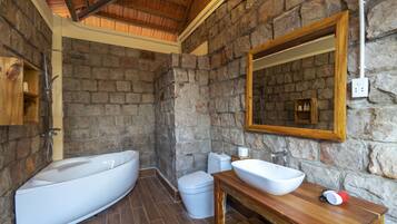 A bathroom with a stone wall, a wooden vanity, a large bathtub, and a toilet.