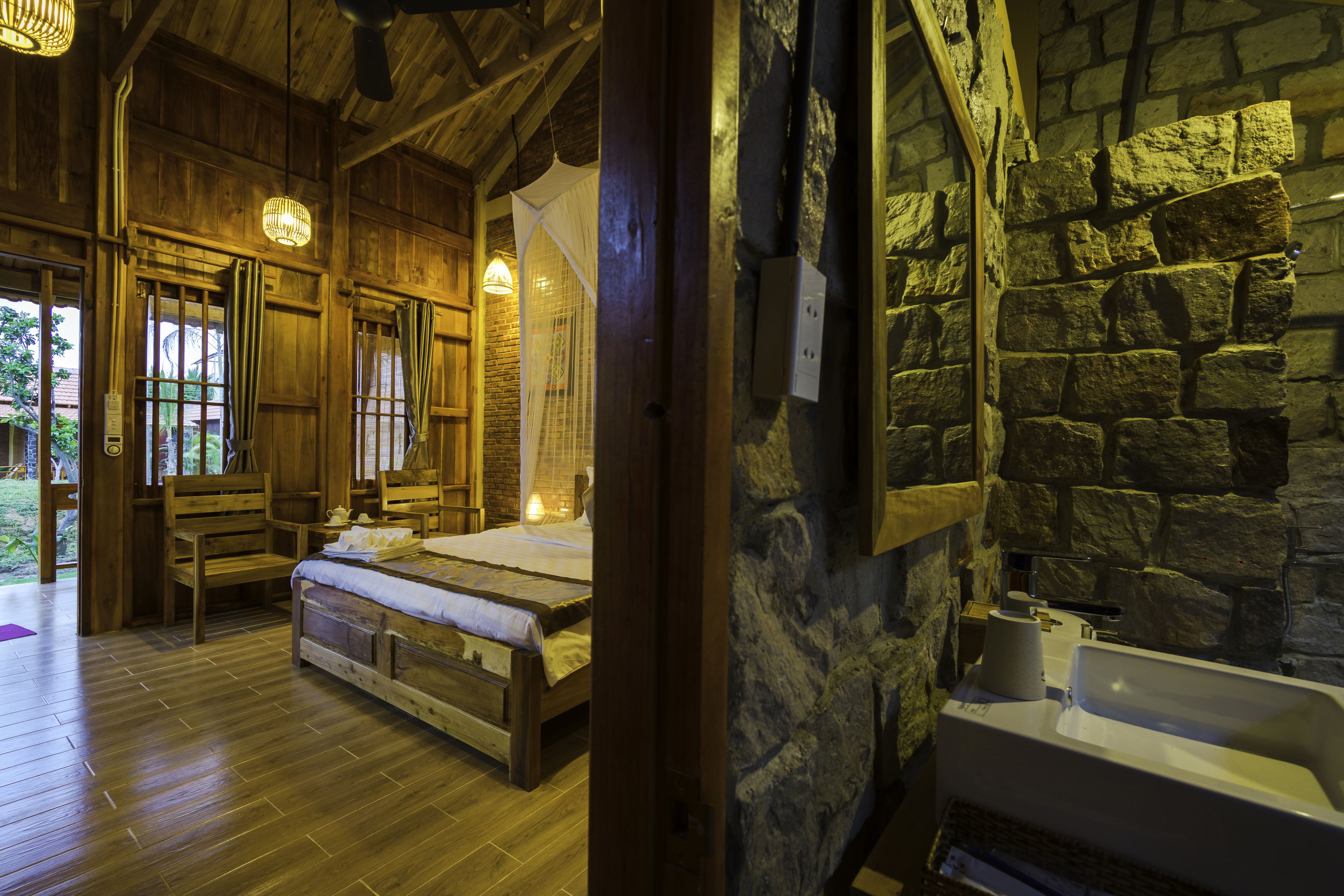 A wooden room with a bed, a stone wall, and a sink.