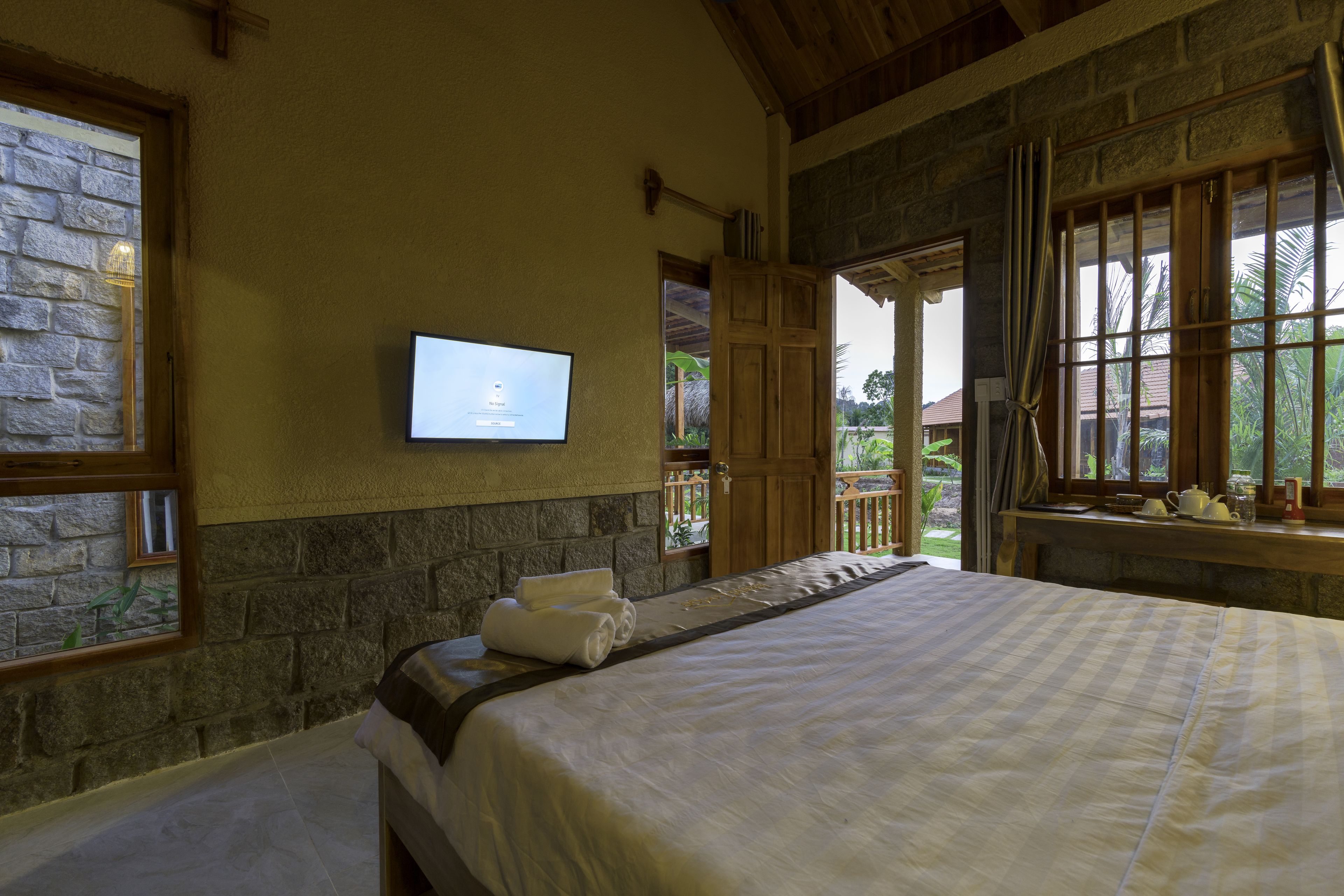 A bedroom with a bed, a television mounted on the wall, and a view of the outdoors through a window.