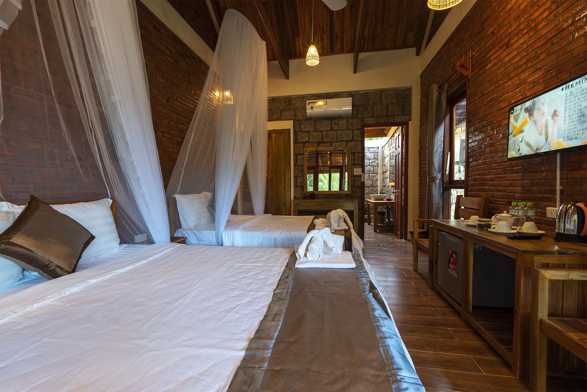 A room with two beds, a wooden desk, and a stone wall.