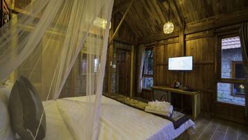 A bedroom with a bed, a television, a wooden desk, and a stone wall.