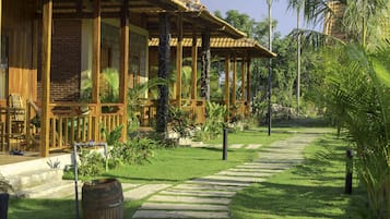 A wooden building with a covered porch, stone pathway, and lush greenery.