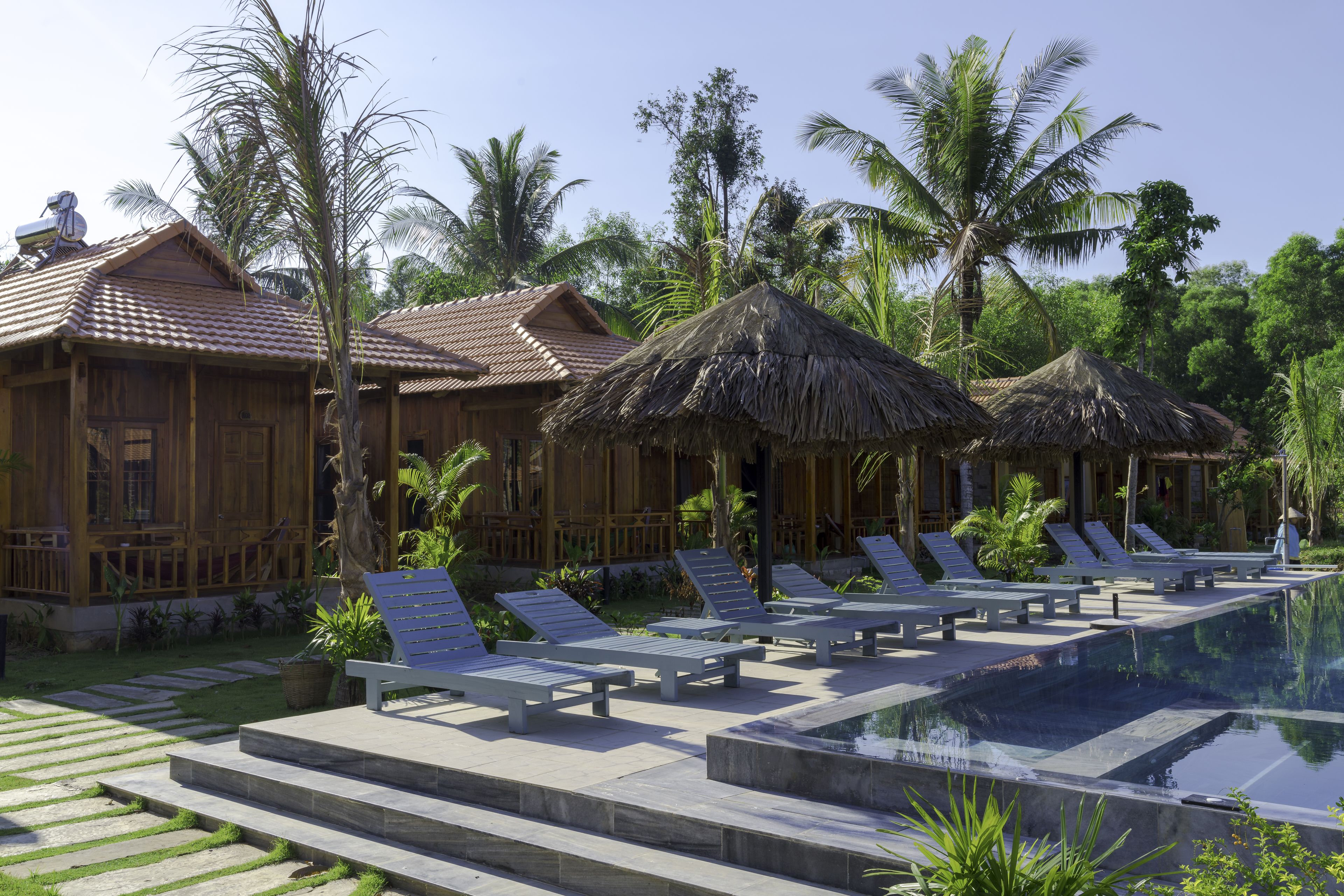 A resort with wooden villas, thatched-roof structures, and a swimming pool with lounge chairs.