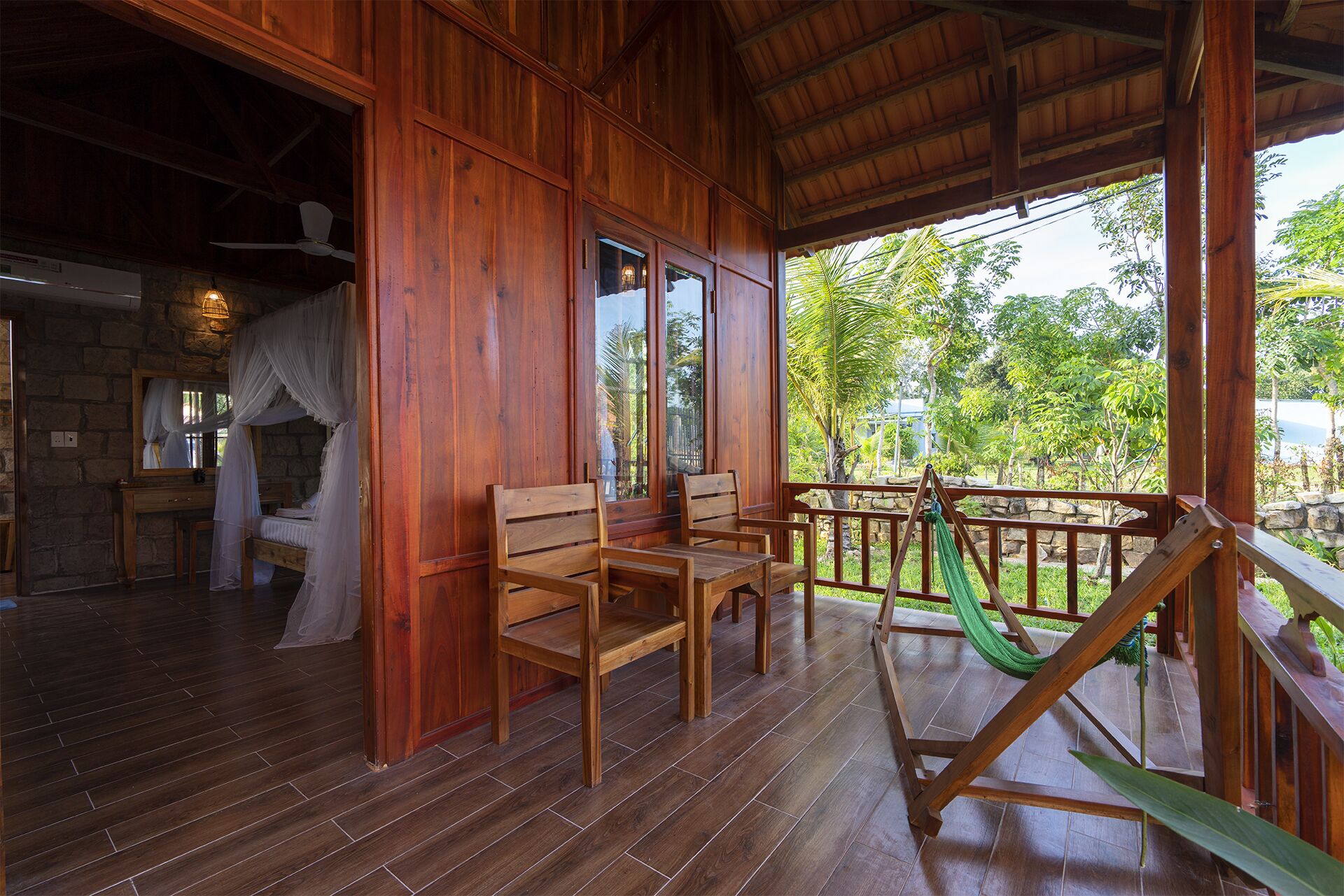 A wooden cabin with a porch, a hammock, and a view of greenery.