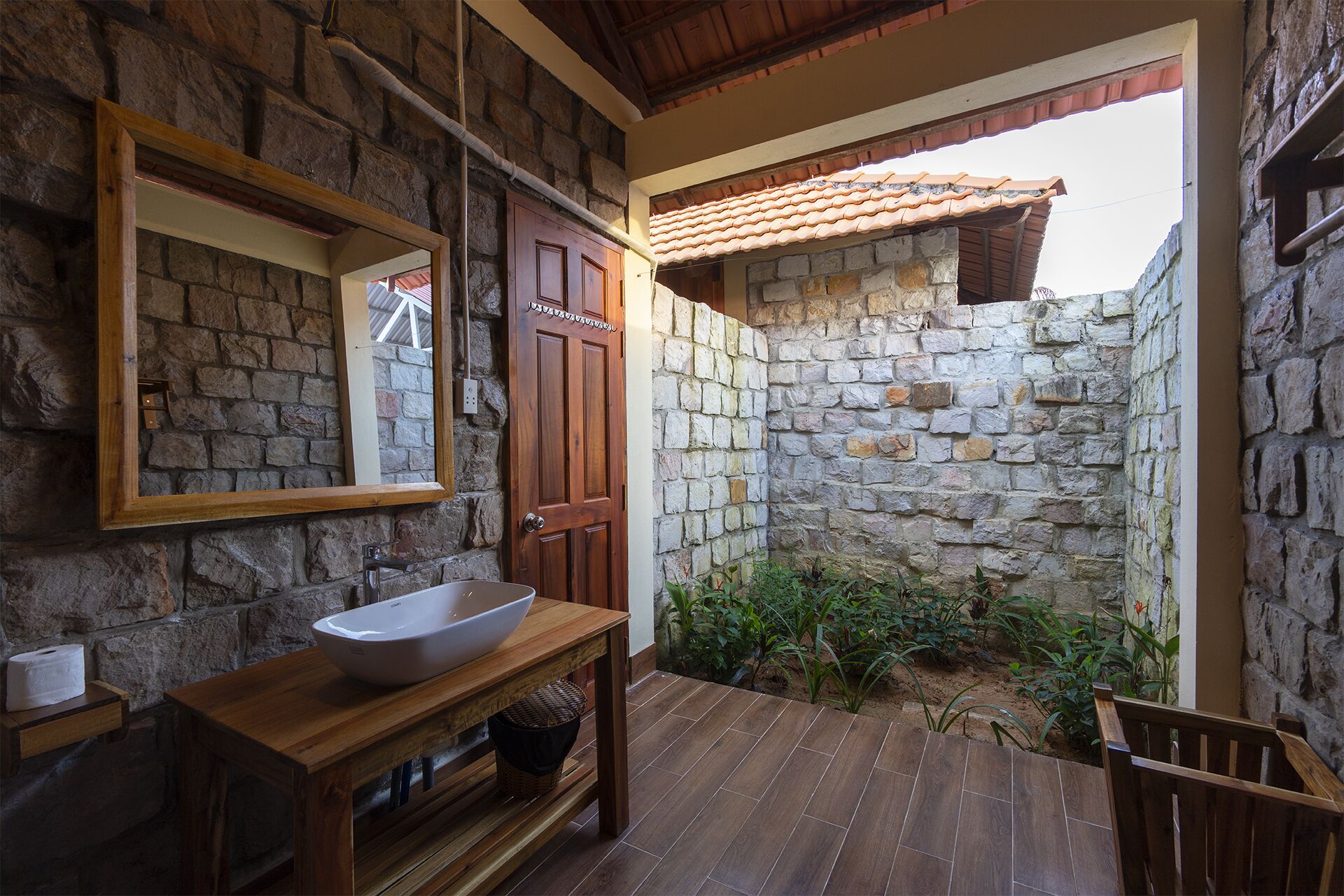 Un baño con paredes de piedra, un tocador de madera, un espejo grande y piso de baldosas.