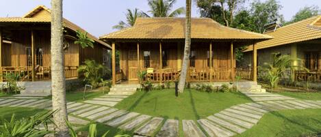 A bungalow-style hotel with a tiled roof, wooden exterior, and a well-maintained lawn with stone pathways.