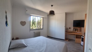 A bedroom with a bed, a window, a radiator, a desk with a TV, and a wardrobe.
