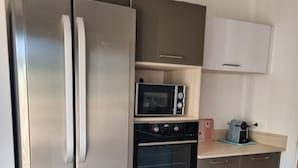A compact kitchen with a stainless steel refrigerator, a microwave, an oven, and a toaster.