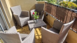 A balcony with wicker furniture, a potted plant, and a view of greenery.