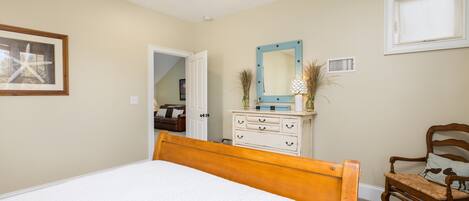 Un dormitorio con una cama de madera, un aparador, una silla y un espejo en la pared.