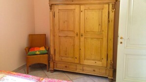 Ein Zimmer mit einem Holzkoffer, einem Korbstuhl mit Kissen und einer weißen Tür.