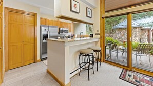 A modern kitchen with wooden cabinets, stainless steel appliances, and a large island with stools. - Hot Tub Views Family Bunks Walk to Chair 20 (Vail)