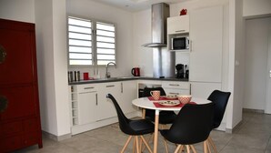 Une cuisine moderne avec des armoires blanches, une hotte en acier inoxydable et un coin repas comprenant des chaises noires et une table blanche.