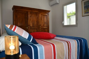 Un dormitorio con cama, almohadas, una lámpara de noche, un armario de madera y una ventana.