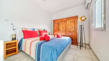 A hotel room with a bed, a wooden wardrobe, a standing lamp, and an air conditioning unit.
