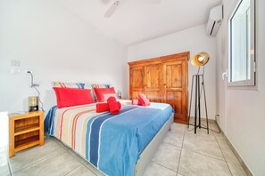 A hotel room with a bed, a wooden wardrobe, a standing lamp, and an air conditioning unit.
