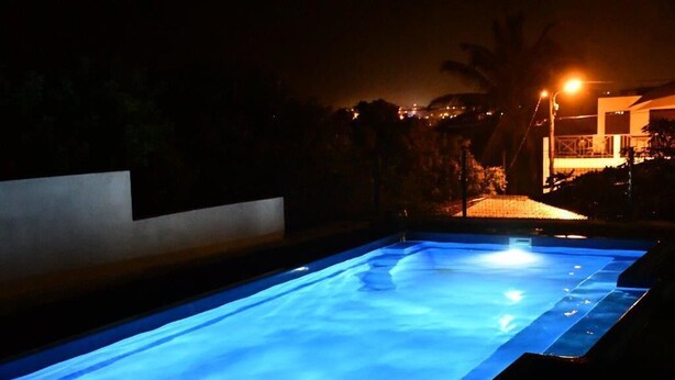 Une piscine la nuit, avec de l’eau illuminée, entourée d’un paysage sombre et d’un bâtiment éclairé en arrière-plan.