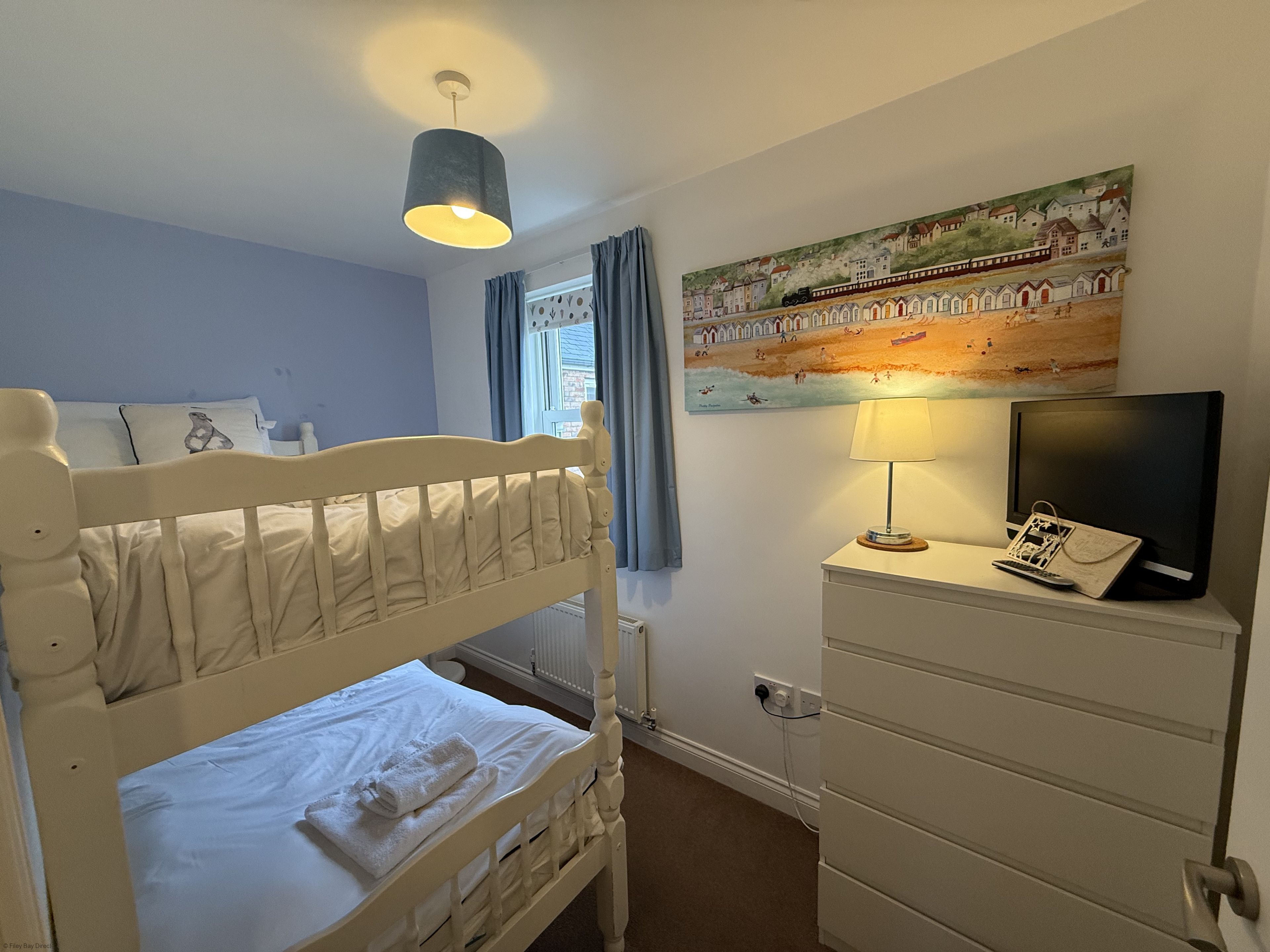 A bedroom with a bunk bed, a dresser, a television, and a painting on the wall.