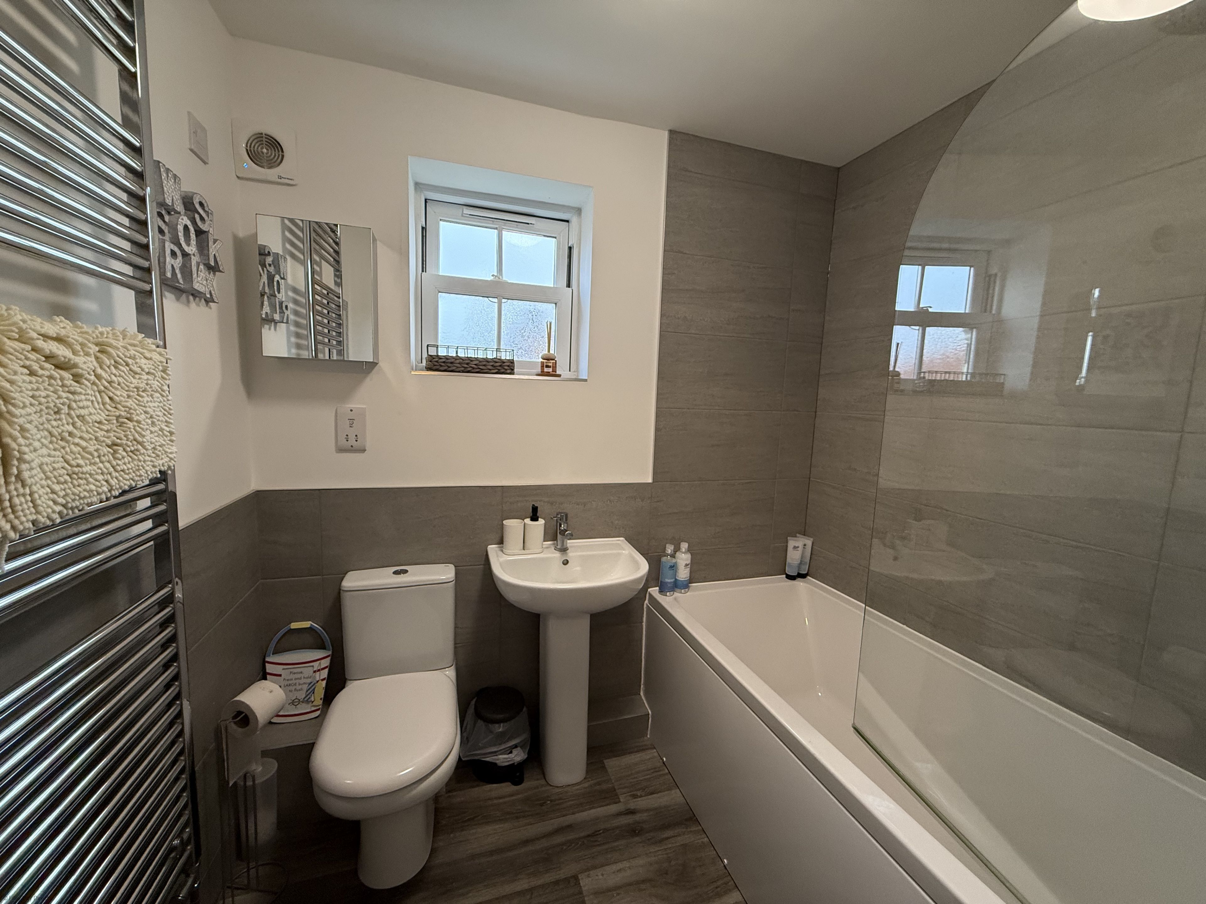 A modern bathroom with a toilet, sink, and bathtub. There is a window above the sink and a towel rack with a towel on it.