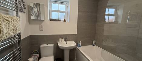 A modern bathroom with a toilet, sink, and bathtub. There is a window above the sink and a towel rack with a towel on it.