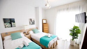 Une chambre d’hôtel avec deux lits, une télévision, une plante et des œuvres d’art accrochées aux murs.
