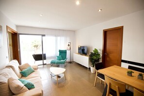 A modern living room with a sofa, a coffee table, a dining table, a TV, and a large window.