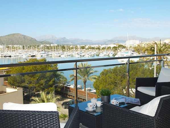 A balcony with wicker furniture, a table with cups and a menu, and a marina with boats in the background. - Cozy fit. brand new, terrace, sea view aircon (Port d´Alcudia)