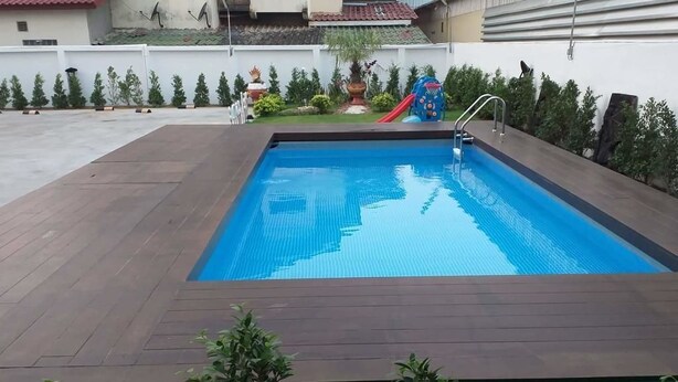 A rectangular swimming pool with a wooden deck, surrounded by greenery and a slide. - Avalon residence2 (Savannakhet)