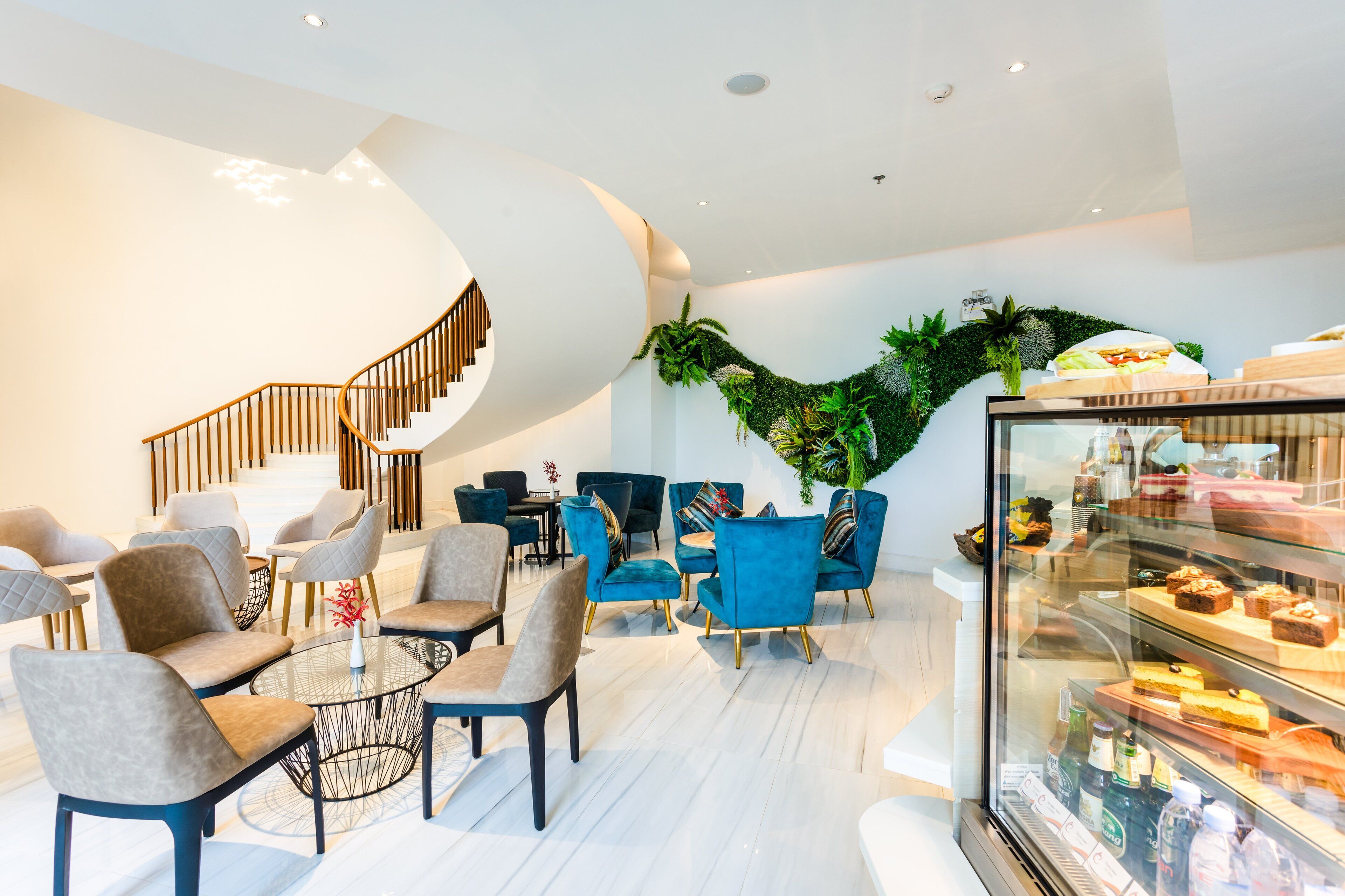 A modern interior with a staircase, seating area, and a display case with desserts.