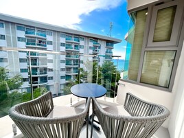 Un balcón con sillas de mimbre y una mesa, con vistas a un edificio moderno con varios balcones y una vista despejada del mar.