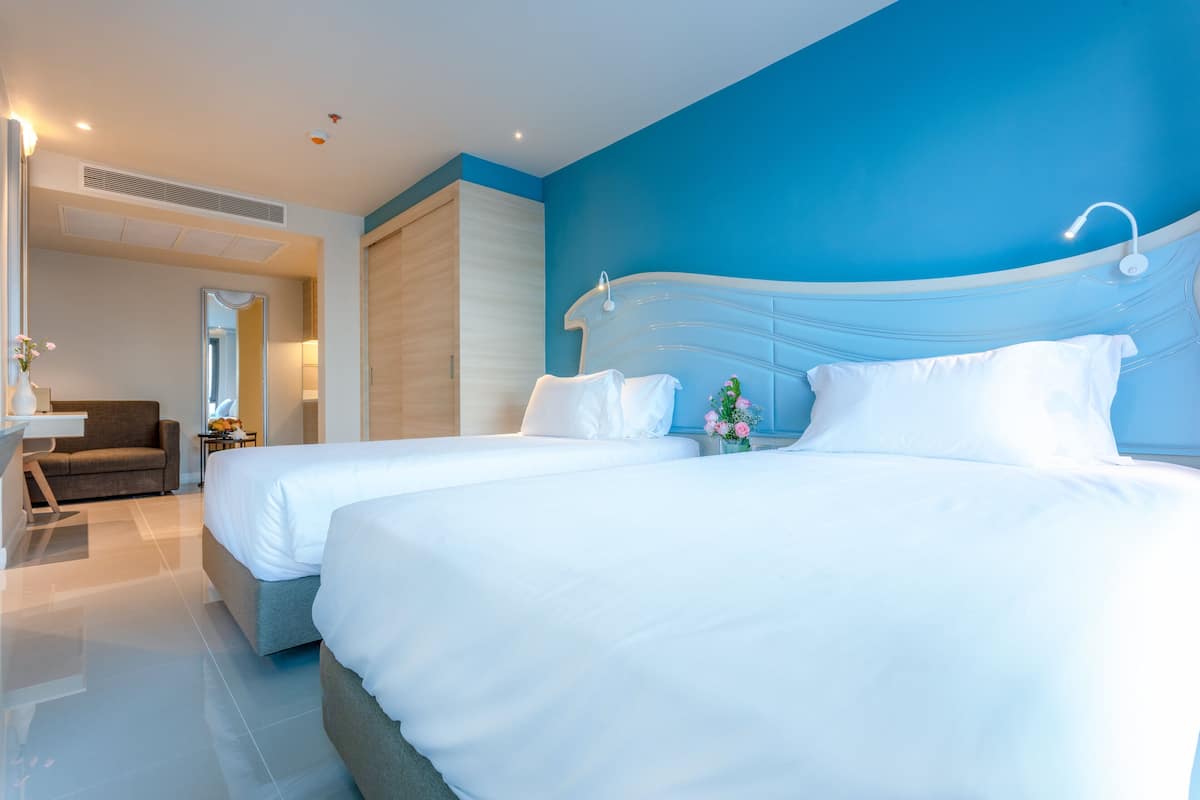 Ett modernt hotellrum med två sängar, en soffa och ett badrum med en blå accentvägg.