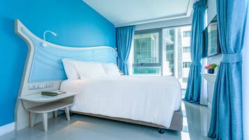 A modern hotel room with a large bed, a bedside table with a lamp, and a view of the city through large windows.