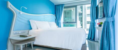 A modern hotel room with a large bed, a bedside table with a lamp, and a view of the city through large windows.