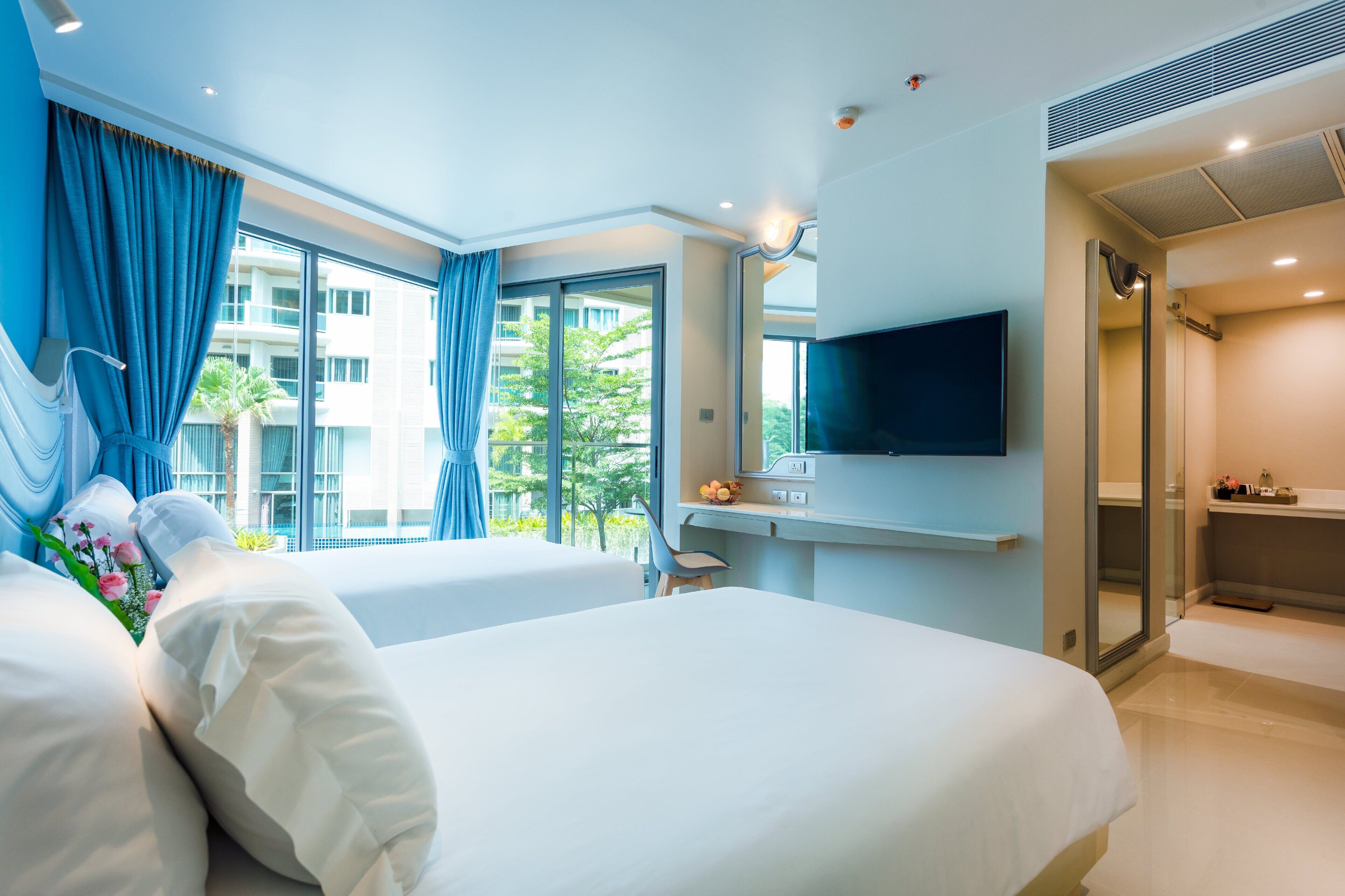 A hotel room with two beds, a desk, a TV, and a bathroom.