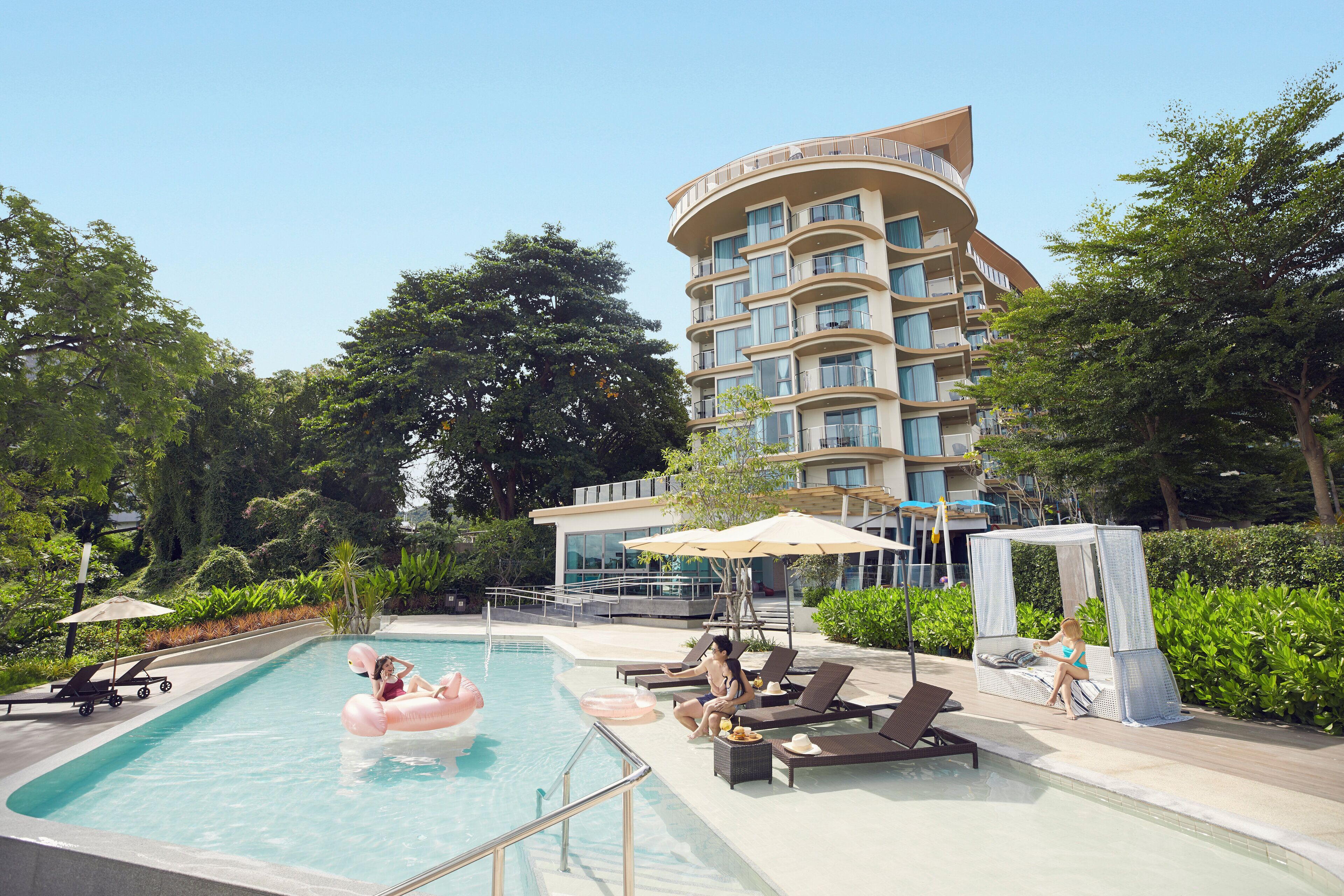 A pool area with lounge chairs, a floating pool float, and a building with balconies.