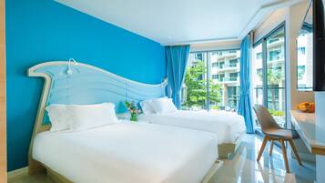 A hotel room with two beds, a large window with a view of a building, and a small table with fruits.