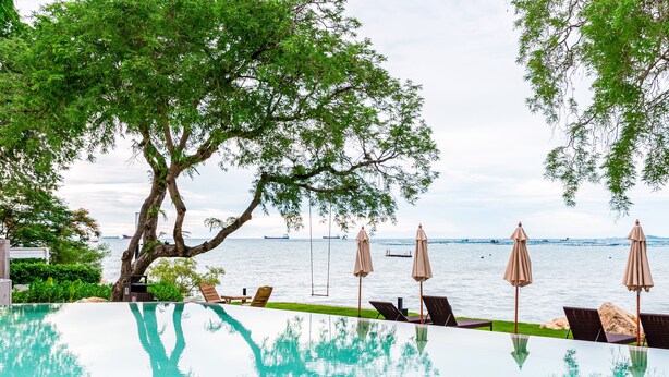 Una piscina infinita con vista despejada al mar, rodeada de sillones y sombrillas.