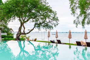 An infinity pool with a clear view of the sea, surrounded by lounge chairs and umbrellas. - Centara Sonrisa Residences & Suites Sriracha (Si Racha)