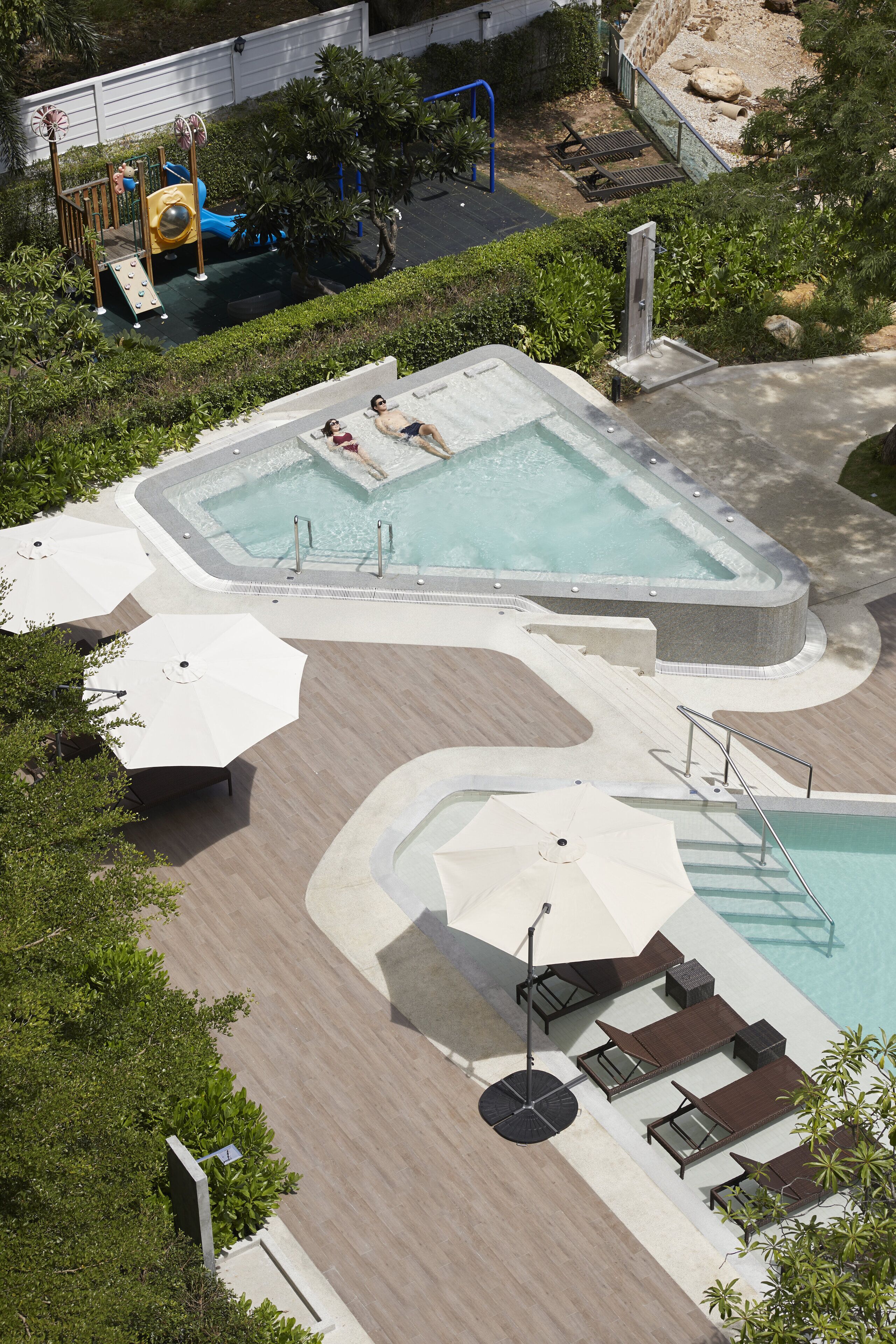 A rooftop pool area with a hot tub, lounge chairs, and umbrellas.