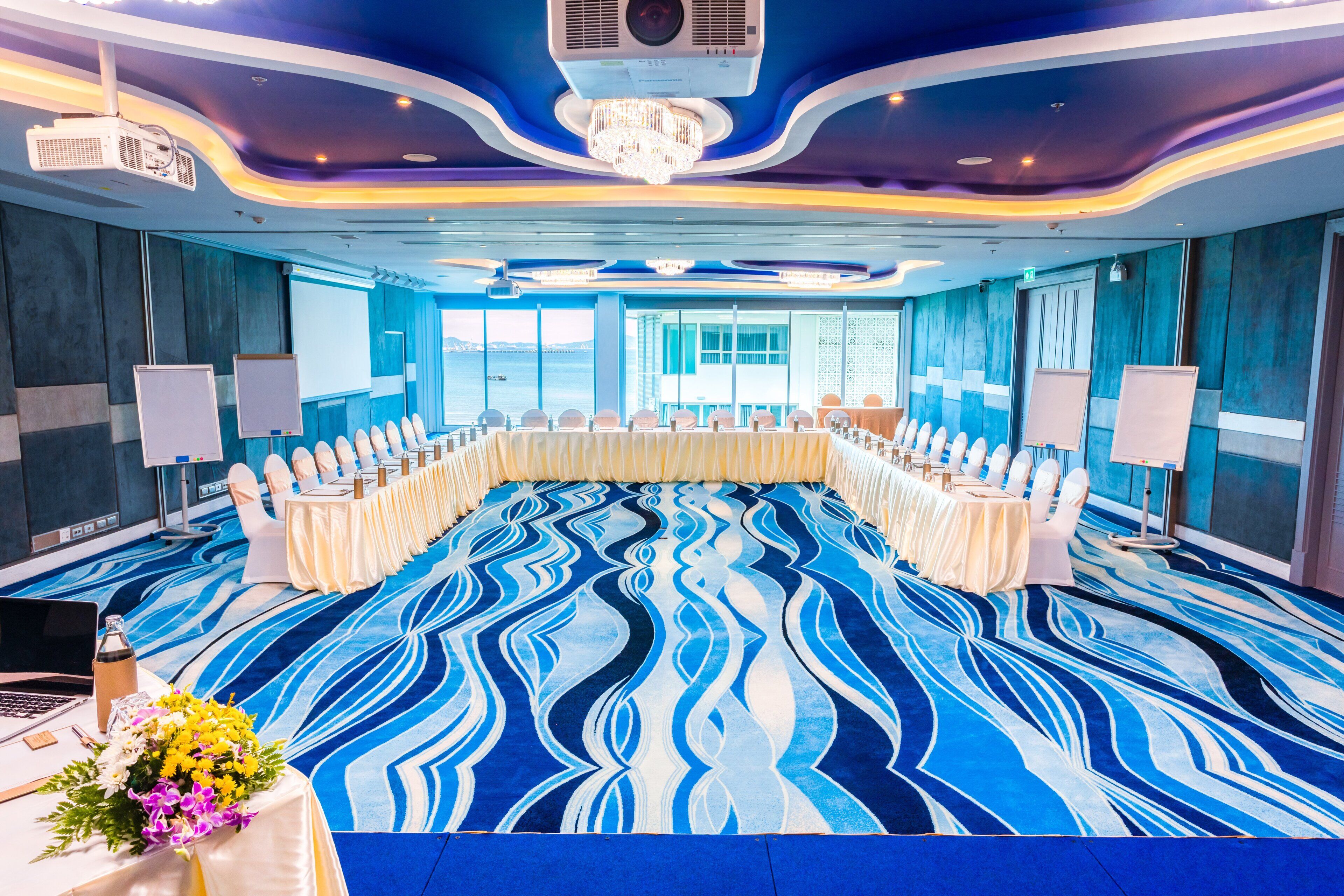A conference room with a long table, white chairs, and a blue carpet.