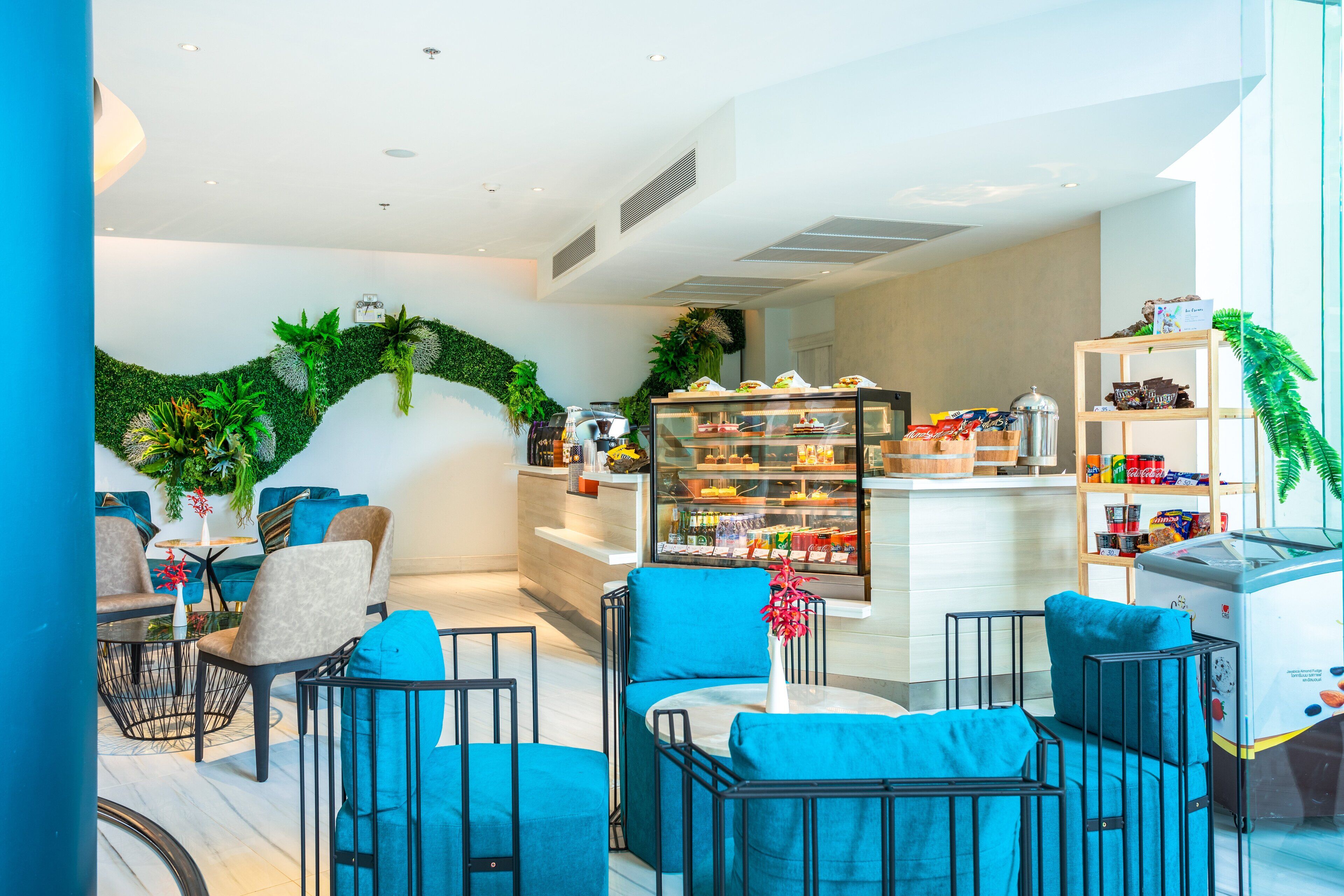 A modern lounge area with blue upholstered chairs, a coffee station, and a display case with snacks.