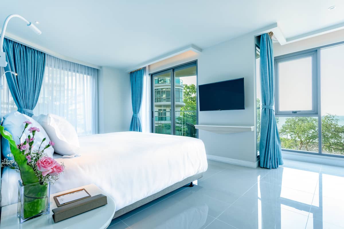 Ett modernt hotellrum med en stor säng, ett nattduksbord med en vas med blommor, en platt-TV som är monterad på väggen och ett stort fönster med utsikt över staden.