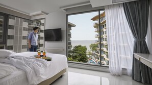Una habitación de hotel moderna con una cama grande, un televisor montado en la pared y un balcón con vista al mar.