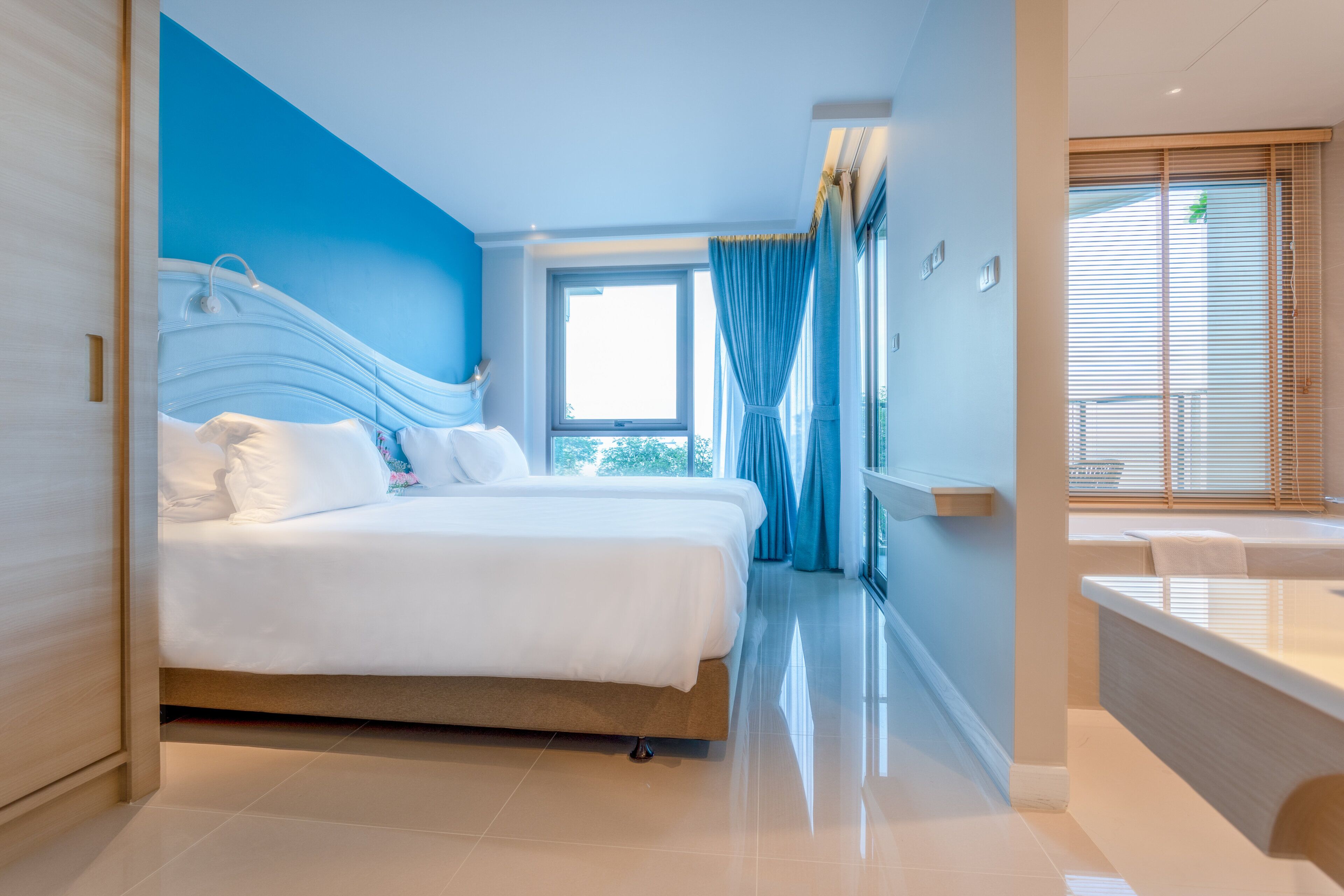 A modern hotel room with a large bed, a bathroom with a bathtub, and a view of the outdoors.