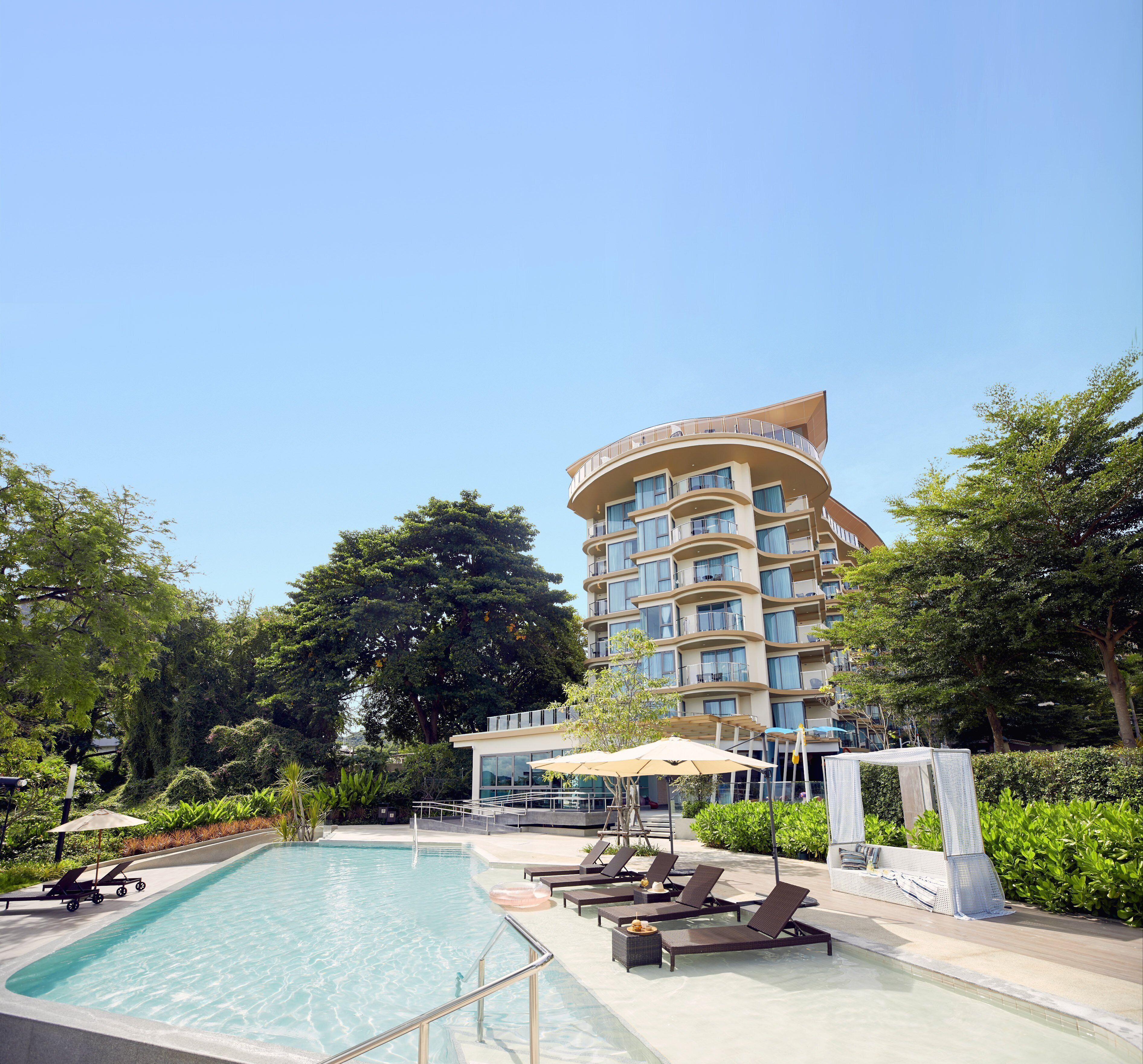 A hotel with a pool, lounge chairs, and a large tree.