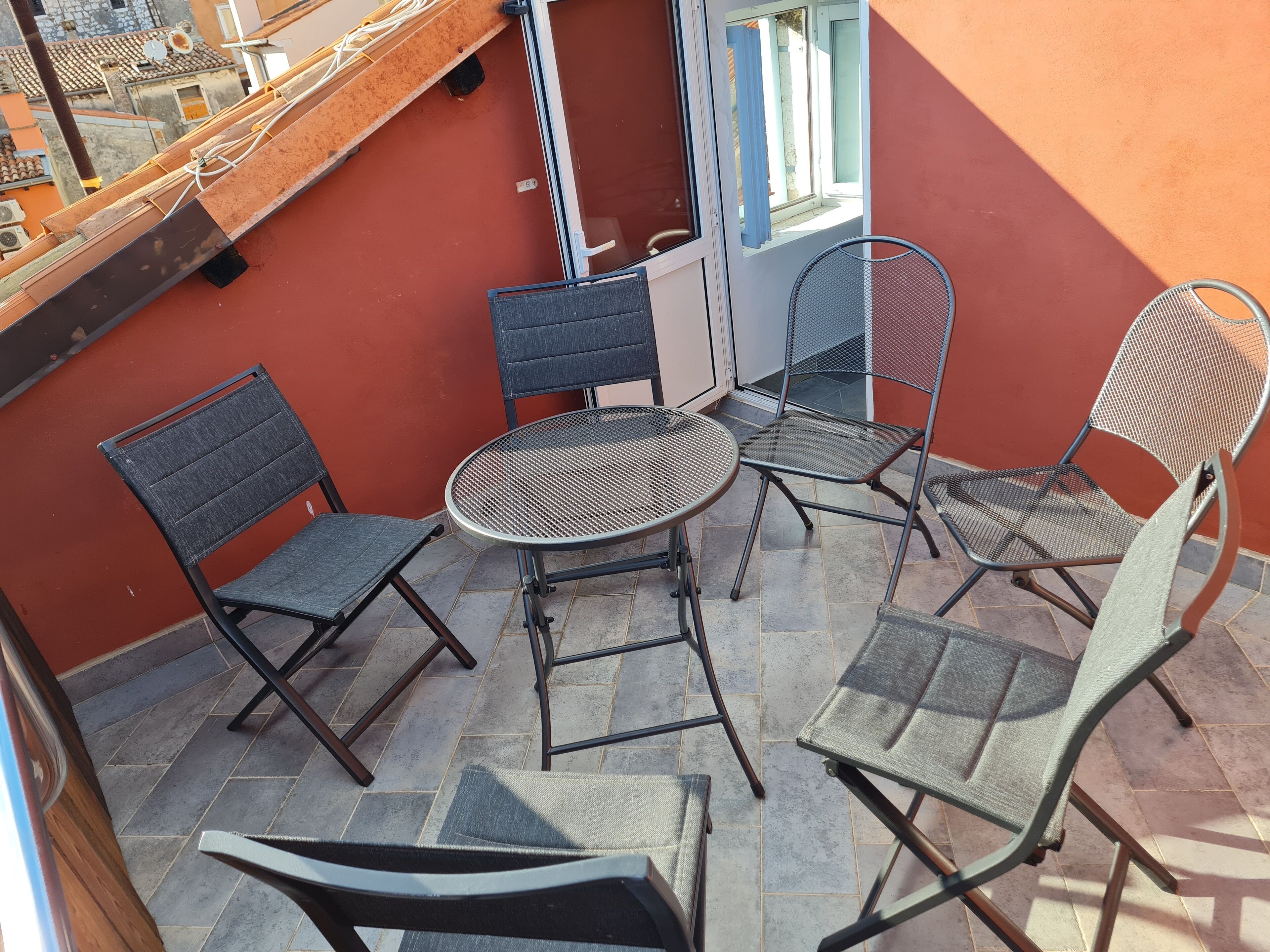 A balcony with four chairs and a small round table, a sliding glass door, and a view of the cityscape.