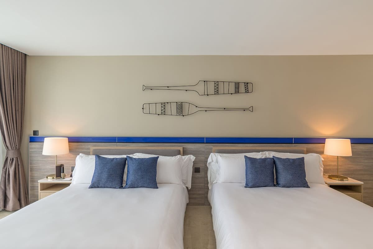 Ein Hotelzimmer mit zwei Betten, einer blauen Akzentwand und Wandlampen.
