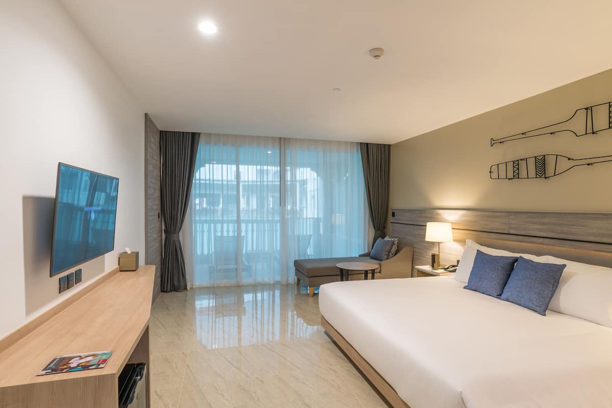 Ein Hotelzimmer mit einem großen Bett, einem Fernseher, einem Schreibtisch, einem Stuhl und einem Vorhangfenster.