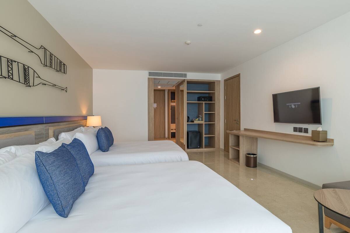Ein Hotelzimmer mit zwei Betten, einem Fernseher, einem Schreibtisch und einem Kleiderschrank.