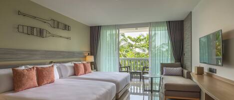 A hotel room with a large bed, a desk, a chair, and a balcony with a view of greenery.